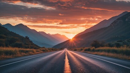 Naklejka premium Serene asphalt road leading towards majestic mountains under a vibrant sunset creating a picturesque travel destination scene.