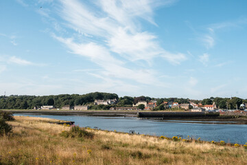 Berwick upon Tweed UK: 3rd Aug 2024: Scenic river landscape with quaint village under a bright blue sky during daytime. River Tweed