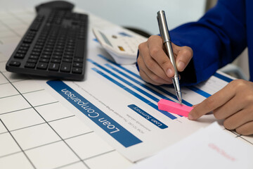 A person is writing on a piece of paper with a pen. The paper has a loan comparison chart on it
