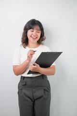 Fototapeta premium Beautiful young asian woman with wavy hair wearing white shirt is holding a black clipboard and writing something using ballpoint pen, isolated over white background.