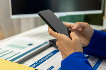 A woman in a blue suit is looking at her phone while reading a piece of paper. She is focused on her phone and the paper, possibly working or studying
