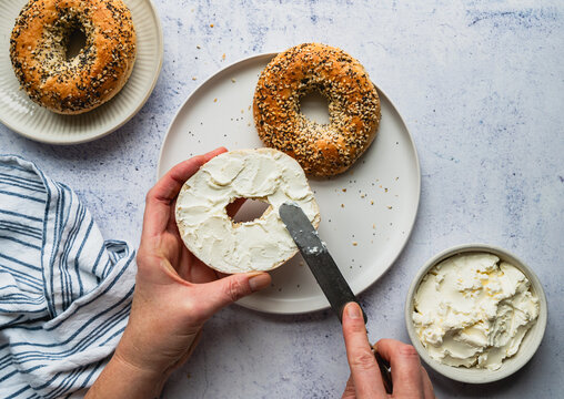 Top view of hands spreading cream cheese on everything bagel.
