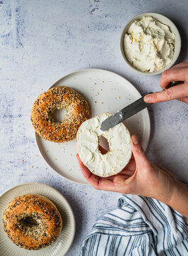 Top view of hands spreading cream cheese on everything bagel.
