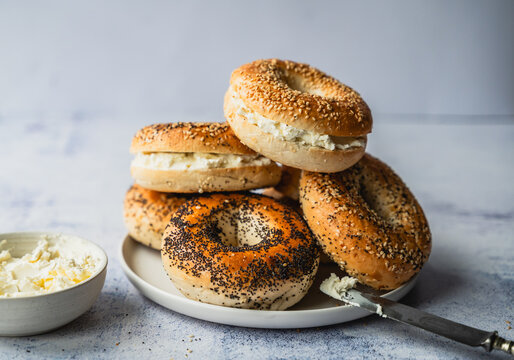 Pile of assorted bagels with cream cheese on light background.