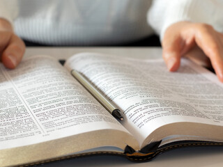 Fototapeta premium Christian woman is holding open holy bible book in her hands while studying and reading. Close-up. Selective focus. Biblical education concept.