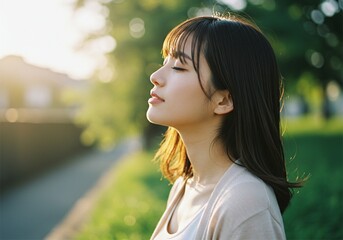 Naklejka premium Portrait of a young woman with closed eyes, enjoying the warm glow of the golden sunset in nature. A peaceful and serene moment captured with soft bokeh background, highlighting relaxation, mindfulnes