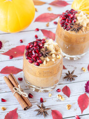 Homemade pumpkin blended drink with pomegranate, cinnamon spice, and walnuts on wooden table with...