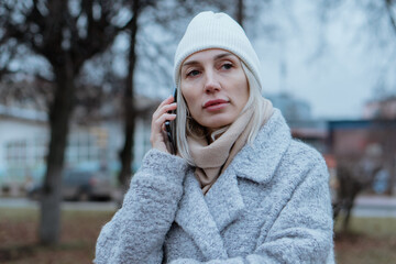 Smiling young woman walking through a frosty city street on a winter morning, talking on her...