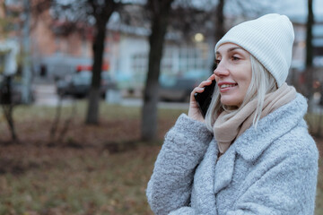 Smiling young woman walking through a frosty city street on a winter morning, talking on her...