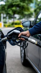 A person is filling up their car with fuel at a gas station on a bright, sunny day, with lush greenery all around