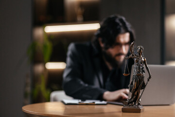 Caucasian male Lawyer, attorney using a laptop, computer in office setting with scales of justice on the desk, judicial technology integration. Legal agreements concept.