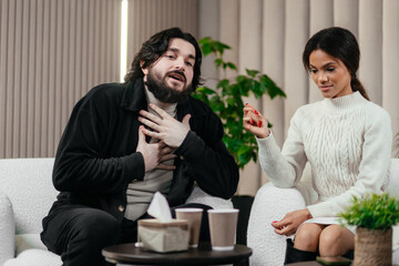 Relationship Crisis. Multiethnic Couple Emotionally Arguing At Home, Suffering Marital Problems, Angry Husband Screaming To Wife With Rage, Upset Woman Sitting On Couch