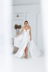 Fototapeta premium Bride in a dress with a train that flutters around on a white background. Stylish trendy wedding 2025