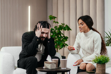 African woman talks to boyfriend about relationship problem on counseling session or couples therapy. Annoyed American man sitting on chair and listening his girlfriend. Psychology concept