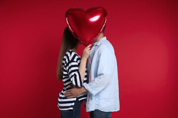 Lovely couple kissing behind heart shaped balloon on red background. Valentine's day celebration
