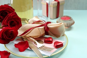 Valentine's day celebration. Romantic place setting with cutlery, hearts and red roses on light blue table, closeup. Space for text