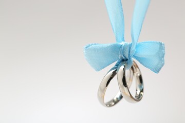 Silver wedding rings tied with ribbon on light grey background, closeup. Space for text