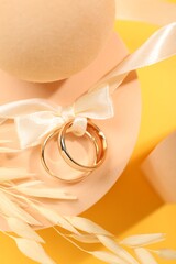 Stylish presentation of wedding rings tied with ribbon on yellow background, top view