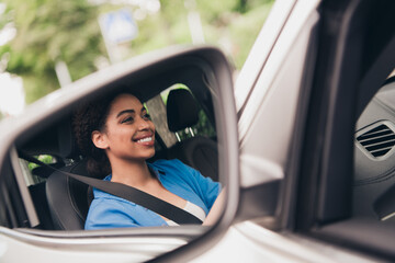 Young woman smiling confidently while driving a car in an urban area during a sunny day, feeling...