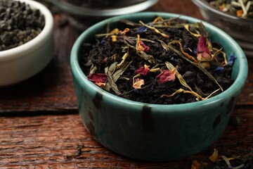 Different dry tea leaves in bowl on wooden table, closeup