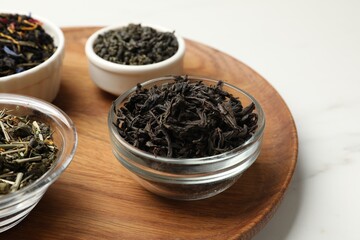 Different dry tea leaves in bowls on white marble table, closeup