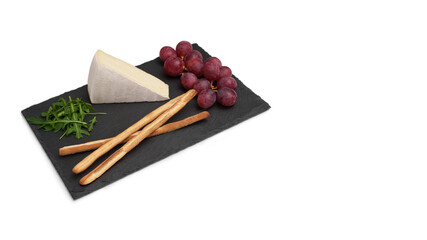Brie cheese with grapes and bread on a black slate board. A snack. Isolated cheese board on a white background.