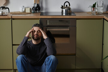 Man sitting on kitchen floor with hands on head in moment of reflection and calmness