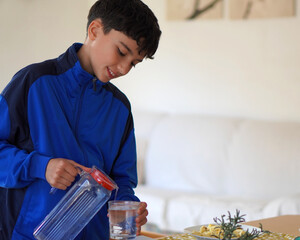 teenage boys and assumption of responsibilities. preteen boy helping at home setting the table and serving water.