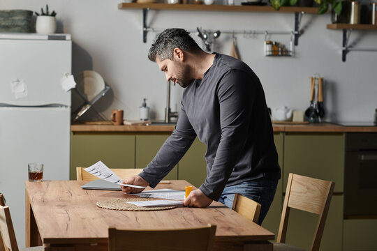 Handsome man reviews paperwork at a modern kitchen table during a tranquil afternoon