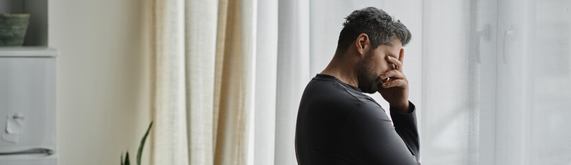 Contemplative moment of a handsome man standing by a window in soft natural light