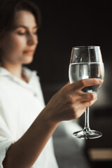 Woman holds glass of water, reflecting her solitude. She appears lost in thought, dehydrated, encapsulating the essence of lonely travel moments.