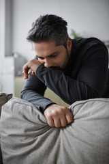 Fototapeta premium Contemplative man resting his chin on a grey couch with intense focus in a serene indoor setting