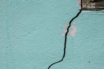 There is a large crack in the cement wall near the window frame of a house.