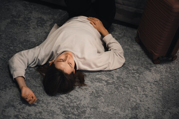 Sad woman sits on the floor, feeling overwhelmed and lonely. Female with suitcase having frustration or after abuse. Dark hotel room with curtains, grief