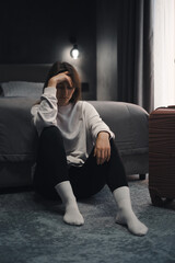 Depressed lonely woman sitting in hotel room with her suitcase nearby. Female emotional crisis...