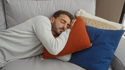 Young man relaxing indoors lying on a couch with colorful pillows in a cozy living room setting.