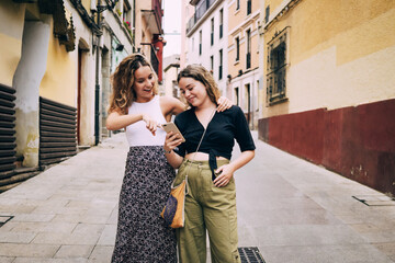 Two young women looking at smartphone walking down the street in Spain
