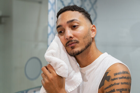 Young man drying his face with a towel in hotel bathroom