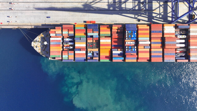 Aerial drone top down photo of industrial cargo container ship being loaded by large cranes in logistics container terminal port
