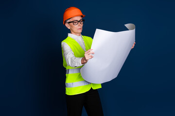 Mature female construction professional in uniform, inspecting blueprints against a dark blue...