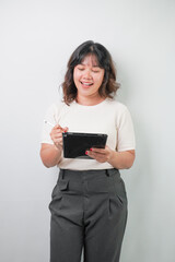 Fototapeta premium Beautiful young asian woman with wavy hair wearing white shirt is writing on a tablet screen using a stylus pen, isolated over white background.