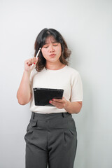 Fototapeta premium Beautiful young asian woman with wavy hair wearing white shirt is thinking while holding a tablet and a stylus pen, isolated over white background.