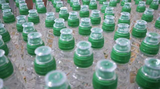 Rows of plastic bottles. Necks of plastic bottles with still mineral water with green  dispenser caps, close up, soft focus