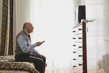 Senior man relaxing on bed while watching television in cozy room