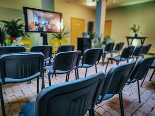 Rows of empty black chairs in a conference room with a blurred background of people engaged in conversation after an event or meeting. Professional and networking atmosphere.
