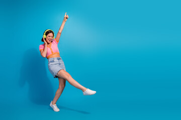 Young woman dancing joyfully with headphones, wearing trendy summer outfit against blue background