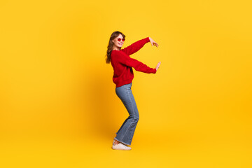 Young woman dancing in vibrant red sweater on yellow backdrop accented with joyful movement and stylish fashion pose
