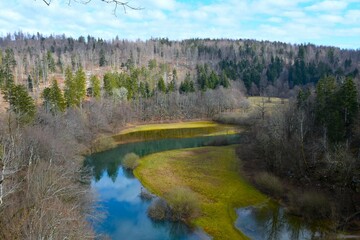 River rak with a meadow on the plains on the shore and a forest on the slopes above and a reflection in the water in Rakov Škocjan nature park in Notranjska, Slovenia