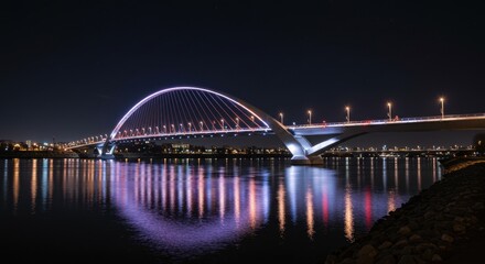 Naklejka premium Modern arch bridge illuminated at night over reflective water in urban landscape
