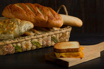 Grilled cheese sandwich on a rustic wooden plate with a basket of bread in the background.